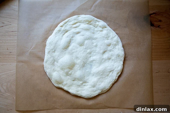 Unlock the Best Sourdough Pizza Crust 13 Stretched round of sourdough pizza on parchment paper.