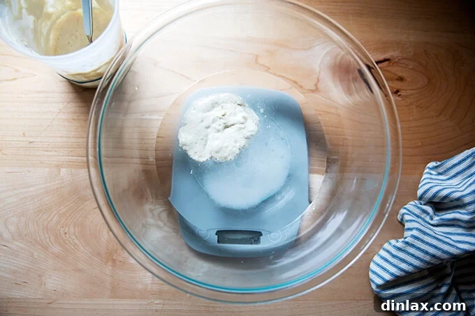 Unlock the Best Sourdough Pizza Crust 4 A bowl filled with water, sourdough starter, and salt on a scale.