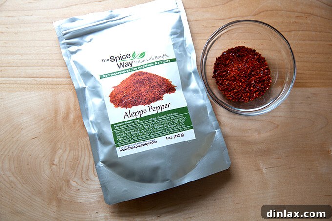 A small bag of Aleppo pepper rests beside an elegant bowl filled with the reddish-brown spice, highlighting its importance in flavoring the dish.