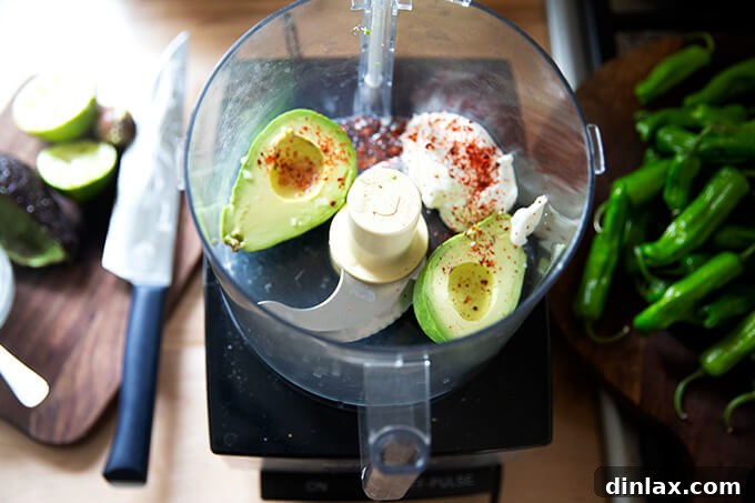A food processor bowl filled with fresh avocado halves, a spoonful of creamy Greek yogurt, and a wedge of juicy lime, ready to be blended into the smooth avocado crema.