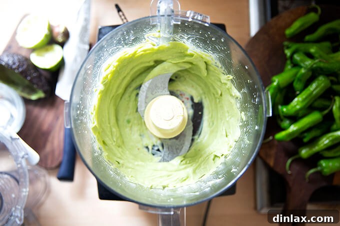 A close-up shot of a food processor bowl, now filled with a perfectly smooth, bright green avocado crema, indicating it's ready for serving.