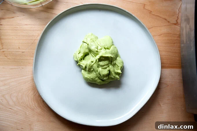 A pristine white platter with a large, creamy spoonful of avocado crema precisely placed in the center, awaiting its artistic spread.