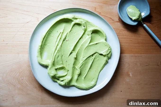 A wide, flat platter artistically spread with a smooth, vibrant layer of avocado crema using the back of a spoon, creating an appealing base for the peppers.
