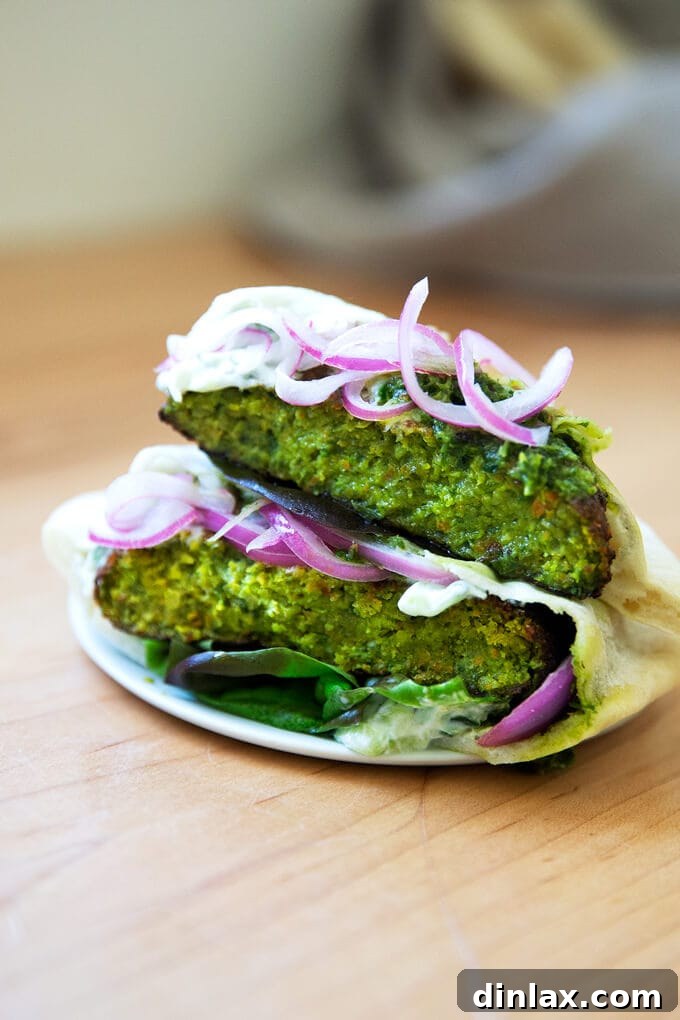 A vibrant plate featuring a whole falafel burger and a halved one, showcasing its textured interior, surrounded by fresh herbs and condiments.