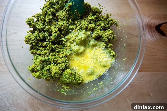 Two beaten eggs being poured into the falafel burger mix in a large mixing bowl.
