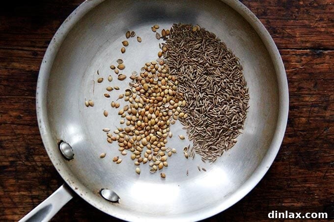A skillet containing whole cumin and coriander seeds toasting over heat.