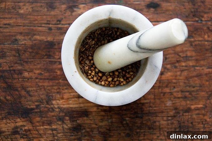 Toasted cumin and coriander seeds being ground in a mortar and pestle.