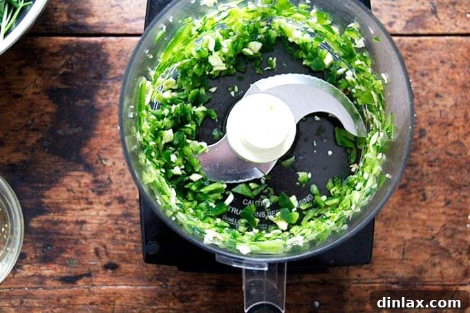A food processor bowl containing roughly puréed chilies and garlic.