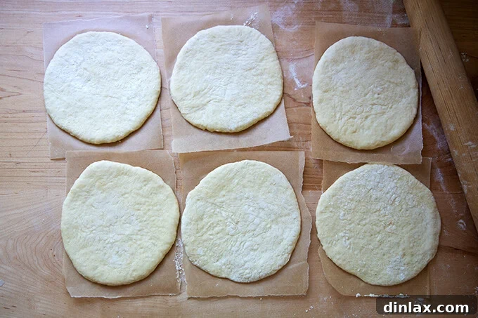 Your Guide to Irresistible Homemade Pita 17 Six rounds of unbaked pita, each placed on a sheet of parchment paper and resting.