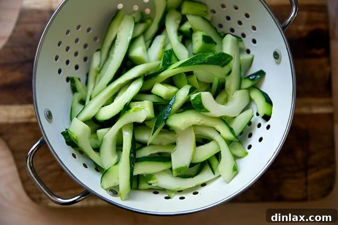 Salted cucumber slices draining in a colander, placed over a bowl to catch excess liquid.