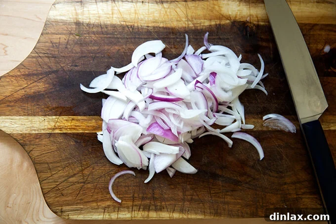 Thinly sliced red onions arranged on a cutting board, adding vibrant color to the preparation.