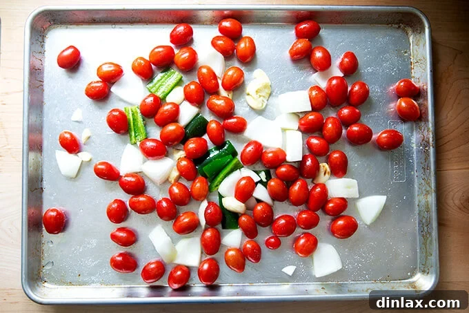 Effortless Homemade Red Enchilada Sauce 4 Tomatoes and roughly chopped onions, garlic, and jalapeño are evenly spread on a sheet pan, seasoned and ready for broiling.