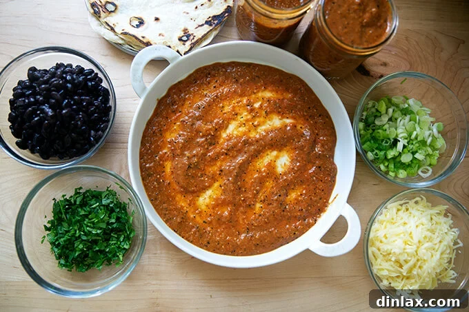 Ultimate Vegetarian Bean and Cheese Enchiladas 3 A baking dish with a thin layer of red enchilada sauce, surrounded by ingredients for black bean and cheese enchiladas.