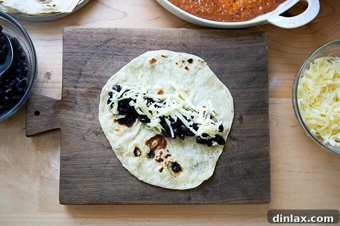 Ultimate Vegetarian Bean and Cheese Enchiladas 4 A flour tortilla on a cutting board, filled with seasoned black beans and grated Monterey Jack cheese.