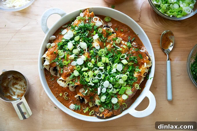Ultimate Vegetarian Bean and Cheese Enchiladas 8 A baking dish filled with sauced enchiladas, topped with vibrant chopped scallions and fresh cilantro.