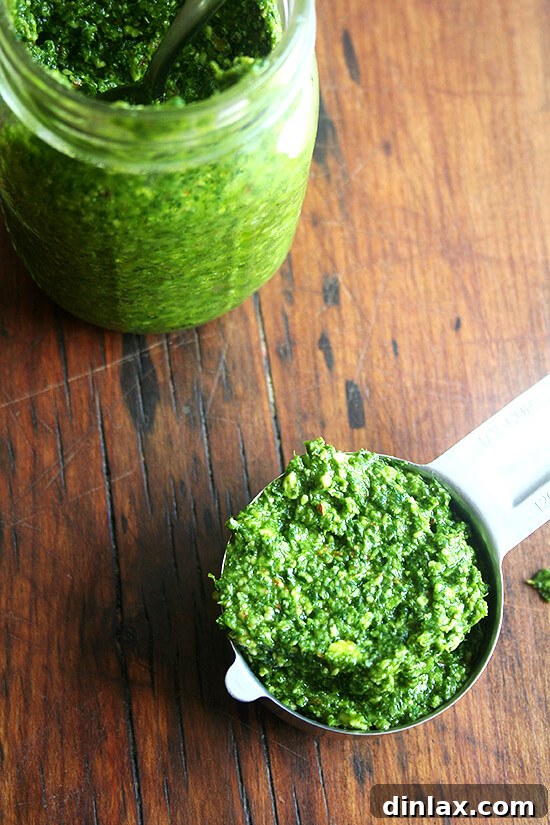 A measuring cup filled with vibrant green pesto sauce, alongside a jar of homemade pesto, highlighting its freshness and readiness for storage or immediate use.