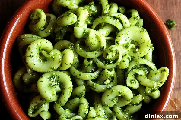 A close-up of a bowl of pasta perfectly tossed with vibrant green pesto sauce, ready to be served.