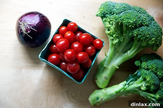 An onion, pint of cherry tomatoes and two heads of broccoli on a kitchen counter.