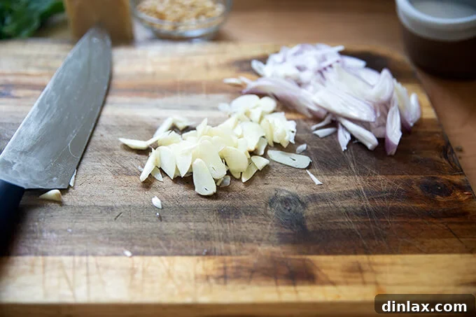 Thinly sliced garlic cloves and shallots neatly arranged on a chopping board, ready to be sautéed for the pasta sauce.