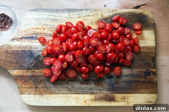 A chopping board filled with a generous amount of halved cherry tomatoes, their vibrant red flesh and juicy interiors exposed, ready to be added to the pasta sauce.