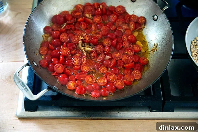 A large skillet on the stovetop filled with a simmering cherry tomato sauce, featuring sautéed shallots, garlic, olive oil, and plump, halved cherry tomatoes, creating a vibrant base for the pasta.