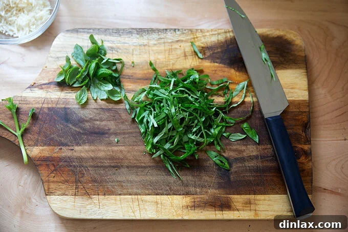 A small pile of vibrant green fresh basil leaves, thinly sliced into ribbons (chiffonade), resting on a wooden chopping board, ready to be added to the pasta.