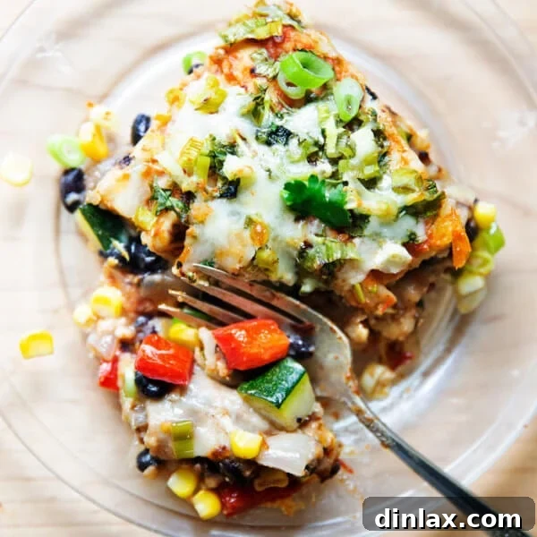 A slice of hearty vegetarian tortilla casserole on a plate, featuring visible layers of tortillas, sautéed vegetables, and melted cheese.