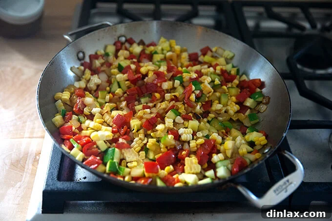 Southwestern Veggie Tortilla Stack 4 A close-up shot of a large skillet on a stovetop, filled with a colorful mix of sautéed summer vegetables including diced onions, red bell peppers, and zucchini, perfectly softened and slightly caramelized.