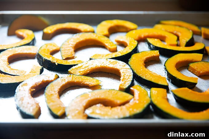 Sliced kobacha squash tossed with olive oil and salt on a sheet pan.