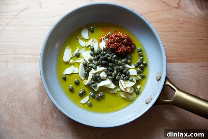 A skillet filled with oil, garlic, capers, and Calabrian chili paste.
