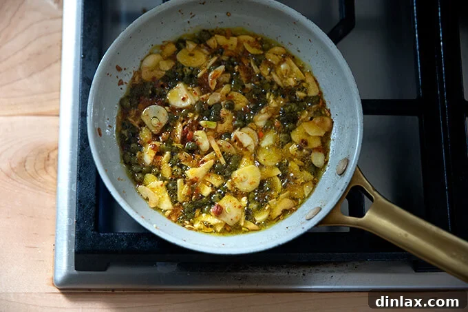 Sizzling oil in a skillet with garlic, capers, and Calabrian chili paste.