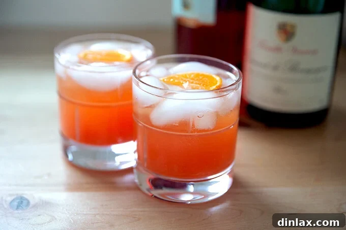 Two glasses of a Tangerine Spritz being completed, with sparkling wine poured over ice, citrus juice, and Campari.