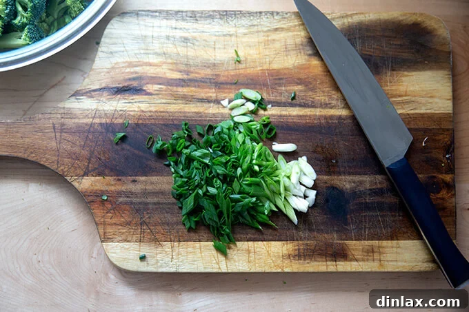 Freshly chopped scallions, both white and green parts, neatly arranged on a wooden board.