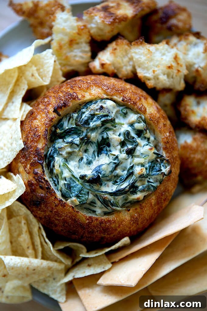A bread bowl filled with spinach artichoke dip, garnished with fresh herbs, ready for serving.