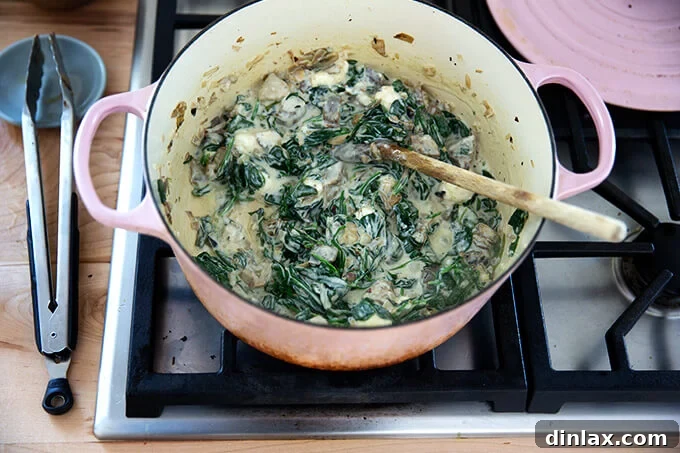 A large pot filled with just-mixed spinach-artichoke dip, creamy and ready for the final cheese.