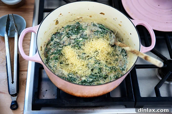 A large pot filled with spinach artichoke dip, with grated Parmesan just added and being stirred.