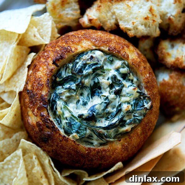 A bread bowl filled with spinach artichoke dip.