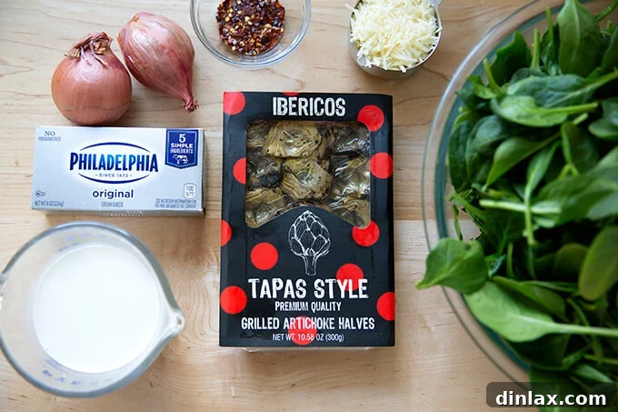 A selection of fresh ingredients including artichoke hearts, spinach, shallots, and cheese, ready for making spinach artichoke dip.