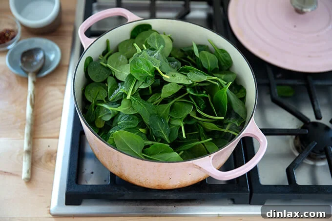 A Dutch oven filled with a generous amount of fresh spinach on top of shallots and artichoke hearts.