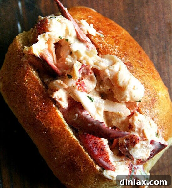A rustic yet elegant homemade lobster roll, generously filled with luscious lobster meat and tarragon mayonnaise on a soft, toasted bun. Fresh lemon wedges and a light garnish complete the presentation.