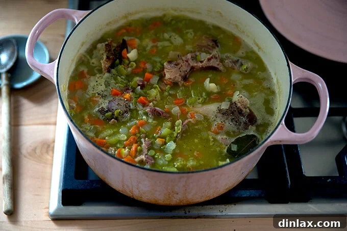 A large pot brimming with a perfectly cooked, thick, and hearty split pea and ham soup, showcasing its comforting, stew-like consistency.