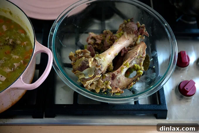 A ham bone, rich with savory juices and clinging bits of meat, carefully removed from the soup and placed in a bowl, ready for carving.