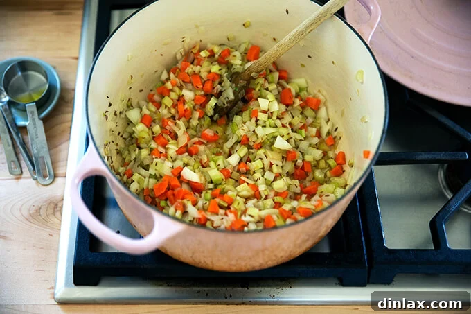 A large pot, covered and simmering gently on low heat, containing sautéed carrots, onions, and celery, softening to perfection before the next steps.