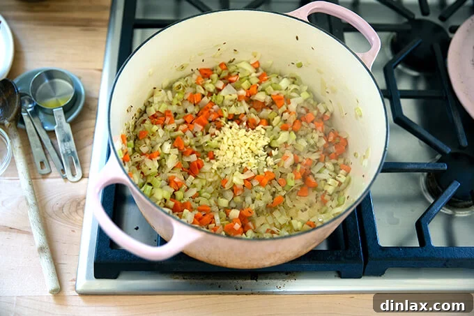 A large pot brimming with beautifully sautéed mirepoix (carrots, onions, celery) now enhanced with fragrant minced garlic, ready for the next additions.