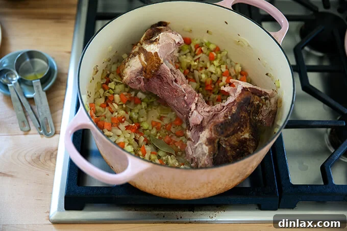 A large pot showcasing sautéed vegetables with a prominent ham bone and a bay leaf, essential for imparting rich flavor to the split pea soup.