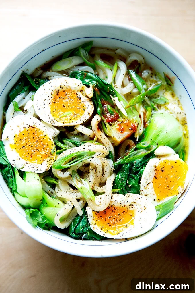 Udon: A Culinary Revelation 2 A vibrant bowl of udon noodles topped with perfectly soft-boiled eggs and a drizzle of hot sauce, embodying a comforting and quick meal.
