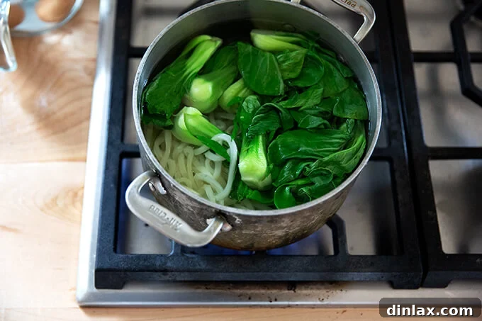 Udon: A Culinary Revelation 8 Udon noodles and vibrant bok choy gently simmering in a pot of boiling water, cooked just until tender for optimal texture.