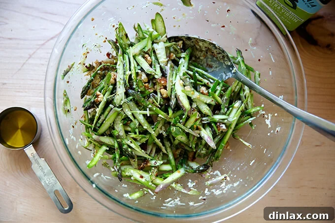 A vibrant raw asparagus salad tossed together in a large bowl, glistening with lemon juice and olive oil, ready for final seasoning.