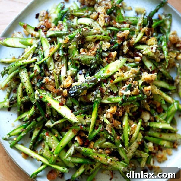 A raw asparagus salad on a platter, garnished with herbs and cheese.