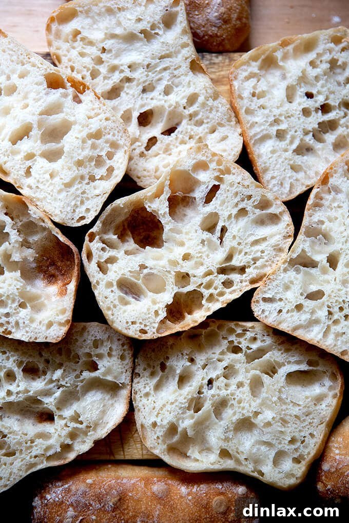 A pile of perfectly halved ciabatta rolls, showcasing their airy, open crumb texture.